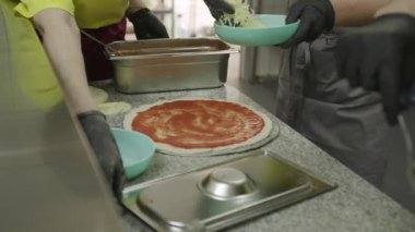 Eldivenli eller pizza hamurunda domates sosuna cömertçe peynir ekliyor.