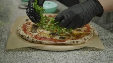 Şefin elleri roka ile pizza süslüyor.