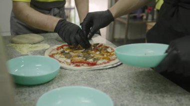 Pizzayı taze malzemelerle süsleyen eller