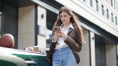 Bir iş kadını dışarıda duruyor, cep telefonu ve kahve ile birden fazla iş yapıyor, kısa bir süre sonra kameraya bağlanıyor.