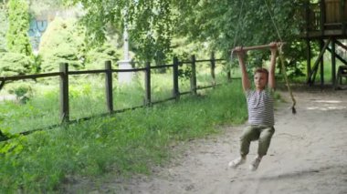 Güneşli bir parktaki bungee 'de sallanan bir çocuk, yaz oyununun heyecanını ve heyecanını yakalıyor, çocukluğun kaygısız anlarının tadını çıkarıyor.