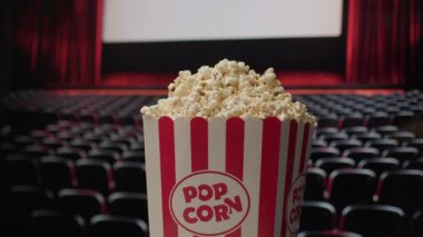 Patlamış mısır sepeti, arka planda sinema perdesi ile döner ve klasik sinema deneyimini vurgulayan dinamik ve sinematik bir atmosfer yaratır.