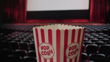 Yakın plan çekimde bir sepet dolusu patlamış mısır çekiliyor. Sinema ortamında, ikonik film izleme deneyimini yeni patlamış, tereyağlı patlamış mısırla vurguluyor.