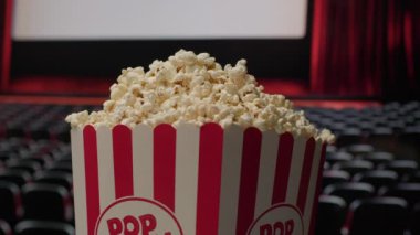 Patlamış mısır sepeti, arka planda sinema perdesi ile döner ve klasik sinema deneyimini vurgulayan dinamik ve sinematik bir atmosfer yaratır.