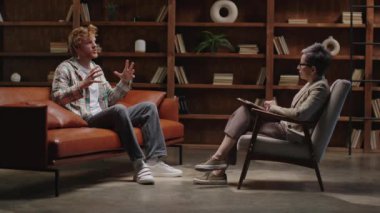 Modern, kitap kaplı ofis ortamında müşterisi olan olgun bir terapist.