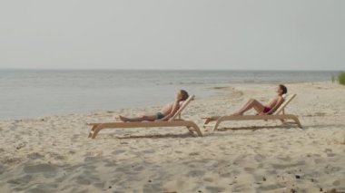 Çocuklar şezlonglara uzanıp sahilde yaz güneşinin tadını çıkarıyorlar. Rahatlatıcı bir tatil anı kaygısız yaz havasını yakalıyor ve deniz kenarında eğleniyor.