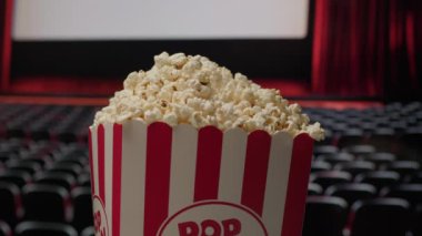 Patlamış mısır sepeti, arka planda sinema perdesi ile döner ve klasik sinema deneyimini vurgulayan dinamik ve sinematik bir atmosfer yaratır.