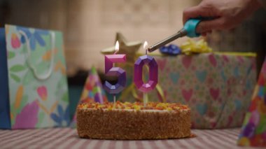 50 numara şeklinde mum hediyelerle çevrili bir doğum günü pastasının üzerinde parlıyor. Şenlikli ve hayat dolu bir sahne tarzında altın bir dönüm noktasını kutluyor.