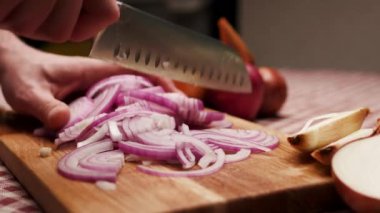 Close-up of a hand cutting a red onion into slices on a wooden chopping board in the kitchen.