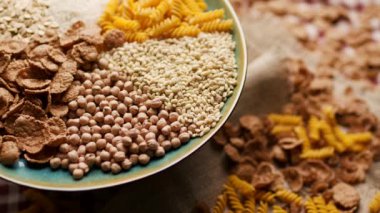 Ekmek, pirinç, kepekli taneler, yulaf, buğday ve mısır makarnası da dahil olmak üzere çeşitli karbonhidrat zengini yiyecekler bir tabakta sergilenmekte ve ahşap bir masada dönmektedir. Beslenme ve sağlıklı beslenme için mükemmel.