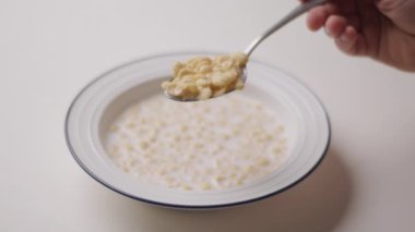 Elinde mısır gevreğiyle kaşığı tutan, süte batırılmış ve yemeye hazır bir elin yakın çekimi. Gevreğin gevrek dokusu açıkça görülüyor.