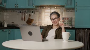 Olgun bir kadın evde otururken bilgisayarından bir video görüşmesi yapıyor. Uzak çalışma temaları, online toplantılar, sanal iletişim ve teknoloji kullanımı için mükemmel