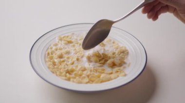 Elinde mısır gevreğiyle kaşığı tutan, süte batırılmış ve yemeye hazır bir elin yakın çekimi. Gevreğin gevrek dokusu açıkça görülüyor.