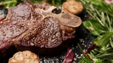 Masanın üzerinde canlı yeşilliklerle çevrili sulu ızgara biftek. Gurme yemekleri, barbekü tarifleri ve yemek tasarım içeriklerini sergilemek için mükemmel.