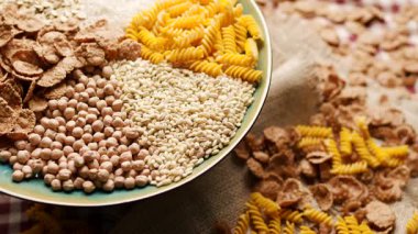 Ekmek, pirinç, kepekli taneler, yulaf, buğday ve mısır makarnası da dahil olmak üzere çeşitli karbonhidrat zengini yiyecekler bir tabakta sergilenmekte ve ahşap bir masada dönmektedir. Beslenme ve sağlıklı beslenme için mükemmel.