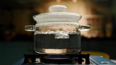 Ocaktaki cam bir tencerede kaynayan suyun yakın plan çekimi, kabarcıklar yükseliyor ve buhar oluşuyor. Yemek, mutfak ve yemek hazırlama için mükemmel..