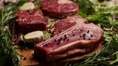 Taze yeşil otlar ve sebzelerle çevrili, tuzlanmış çiğ biftek. Barbekü, aşçılık ve gurme yemek içeriği için mükemmel.