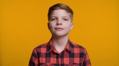 Parlak bir gülümsemesi olan neşeli 10 yaşında beyaz bir çocuk sarı arka plandaki kameraya bakıyor. Neşeli ve pozitif bir portre, çocukluk, mutluluk ve yaşam tarzı içeriği için mükemmel..