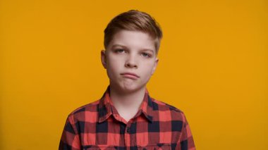 Genç bir çocuk üzgün bir ifadeyle kameraya bakar, derin bir duygu aktarır. Parlak sarı arka plan onun ruh haliyle çelişiyor, duygularını ve yüz ifadesini vurguluyor..