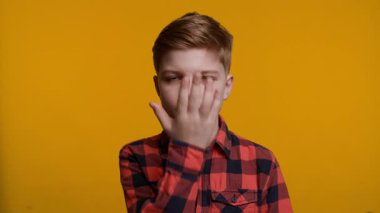 Genç bir çocuk yüzünü klasik bir facepalm jesti ile kapatıyor. Hayal kırıklığını ya da inançsızlığı ifade ediyor. Parlak sarı arka plan onun tepkisini ve duygularını vurguluyor..