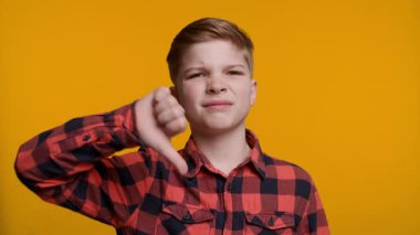 Genç bir çocuk kameraya bakarken onaylamadığını ya da memnuniyetsizliğini dile getiriyor. Parlak sarı arka plan, onun olumsuz hareketleriyle çelişiyor..