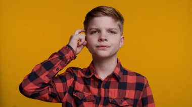 Genç bir çocuk parmağıyla şakağına hafifçe vuruyor, önce düşünmesi gerektiğini işaret ediyor. Onun düşünceli ifadesi parlak sarı arka planla çelişiyor, zekayı ve karar verme mekanizmasını vurguluyor..