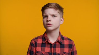 Genç bir çocuk kafasını sağa sola sallayarak ciddi ya da şakacı bir ifadeyle açık bir hayır işareti yapıyor. Parlak sarı arka plan güçlü tepkisini ve vücut dilini vurguluyor..