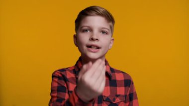 Genç bir çocuk hoş geldin jesti ile elini sallıyor, neşeli görünürken birini içeri davet ediyor. Parlak sarı arka plan onun dostça ve açık ifadesini vurguluyor..