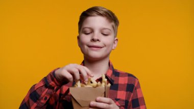 Genç bir çocuk büyük bir zevkle patates kızartması servis etmekten zevk alır. Parlak sarı arka plan, yemek zamanının eğlenceli ve neşeli atmosferini arttırıyor..