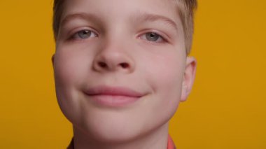 Parlak, neşeli bir gülüşü olan genç bir çocuğun yakın çekimi. Neşeli ifadesi mutluluk ve sıcaklığı canlı sarı arka planda yayıyor..