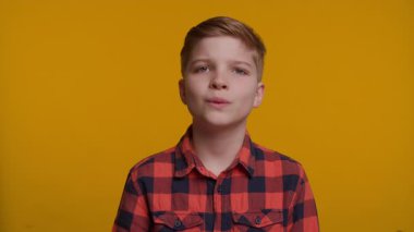 Genç bir çocuk eliyle ağzını kapatarak şaşkınlık ve şaşkınlık ifade eder. Geniş gözleri ve heyecanlı tepkisi parlak sarı arka planda göze çarpıyor..