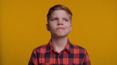 Genç bir çocuk düşünceli bir şekilde yan tarafa bakar, derin düşüncelere dalır, sonra sıcak bir gülümsemeyle kameraya döner. Parlak sarı arka plan onun değişen duygularını vurguluyor..