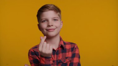 Genç bir çocuk parmaklarını kullanarak sevgi ve şefkat gösteren bir kalp şekli oluşturur. Onun sıcak ve neşeli ifadesi parlak sarı arka plana karşı duruyor..