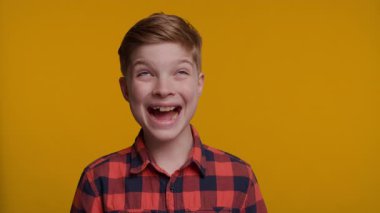 Genç bir çocuk komik ve abartılı bir yüz ifadesi göstererek komik bir surat ifadesi sergiliyor. Onun aptal ve enerjik görünümü parlak sarı arka planda göze çarpıyor..