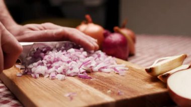 Mutfaktaki ahşap doğrama tahtasının üzerinde kırmızı soğanı dilimleyen elin yakın çekimi..