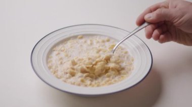 Elinde mısır gevreğiyle kaşığı tutan, süte batırılmış ve yemeye hazır bir elin yakın çekimi. Gevreğin gevrek dokusu açıkça görülüyor.