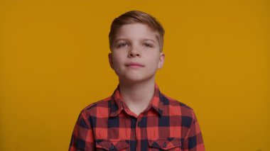 Genç bir çocuk ağzı açık durur, şok ya da şaşkınlık belirtileri gösterir. Geniş gözleri ve dramatik tepkisi parlak sarı arka plana çarpıyor..
