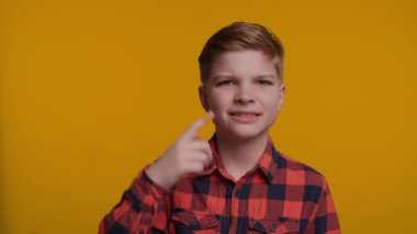 Genç bir çocuk parmağıyla şakağına hafifçe vuruyor, önce düşünmesi gerektiğini işaret ediyor. Onun düşünceli ifadesi parlak sarı arka planla çelişiyor, zekayı ve karar verme mekanizmasını vurguluyor..