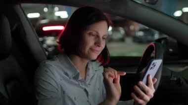 Bir kadın park halindeki arabasında oturuyor, akıllı telefonunu karıştırıyor, aracın içinde bir rahatlama ve bağlantı anını vurguluyor..