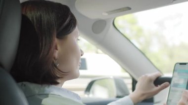 Bir kadın araba kullanırken akıllı telefonuyla mesaj atıyor, direksiyon başında telefon kullanmanın tehlikelerini ve dikkat dağıtıcı unsurlarını vurguluyor..