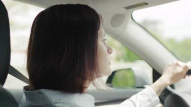 30 'lu yaşlarında araba süren bir kadının yakın çekimi, elleri direksiyonda ve odaklanmış bir yüz ifadesi, yolda bir anlık konsantrasyon yakalamış..