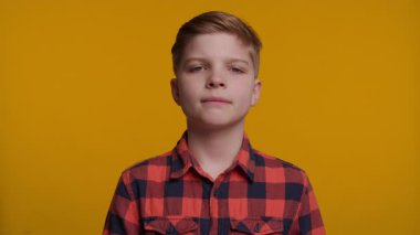 Genç bir çocuk başını arkaya eğiyor, geniş gözlerle bakıyor ve inançsızlık ifadesi sergiliyor. Parlak sarı arka plan onun şaşırmış ve şaşırmış tepkisini arttırır..