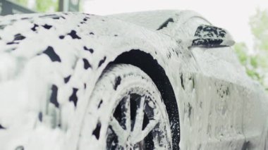 Bir araba, bir oto yıkama istasyonunda tamamen kalın, beyaz köpükle kaplıdır, parlak bir bitiş için temizlik ve detay sürecini vurgular..