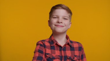 Neşeli genç bir çocuk doğrudan kameraya bakarken başparmağını kaldırıyor. Parlak sarı arka plan, onun kendine güvenen ve mutlu ifadesine enerji ve pozitiflik katıyor..