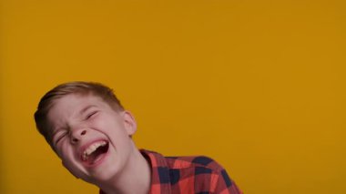 Genç bir çocuk doğrudan kameraya bakıp neşe ve mutluluk saçarak kahkahalara boğuluyor. Parlak sarı arka plan onun neşeli ve bulaşıcı ifadesini arttırır..