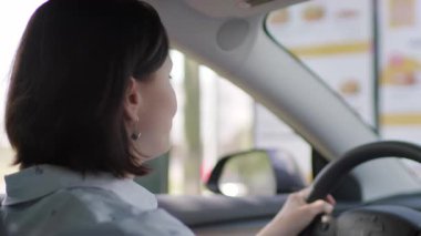 Bir kadın arabasında oturur ve hoparlörden yemek sipariş eder. Tipik bir fast-food anını rahatlık ve beklentiyle yakalar..