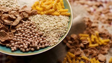 Ekmek, pirinç, kepekli taneler, yulaf, buğday ve mısır makarnası da dahil olmak üzere çeşitli karbonhidrat zengini yiyecekler bir tabakta sergilenmekte ve ahşap bir masada dönmektedir. Beslenme ve sağlıklı beslenme için mükemmel.