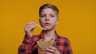 Genç bir çocuk büyük bir zevkle patates kızartması servis etmekten zevk alır. Parlak sarı arka plan, yemek zamanının eğlenceli ve neşeli atmosferini arttırıyor..