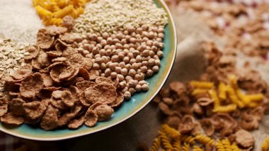 Ekmek, pirinç, kepekli taneler, yulaf, buğday ve mısır makarnası da dahil olmak üzere çeşitli karbonhidrat zengini yiyecekler bir tabakta sergilenmekte ve ahşap bir masada dönmektedir. Beslenme ve sağlıklı beslenme için mükemmel.