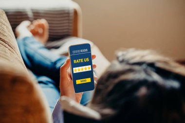 Evde ürün ve hizmetleri değerlendirmek için cep telefonu kullanan bir kadın.